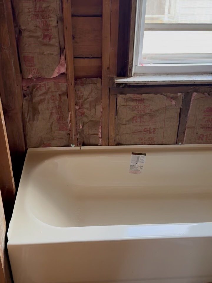After: a new white bathtub set in a framed bathroom under a window