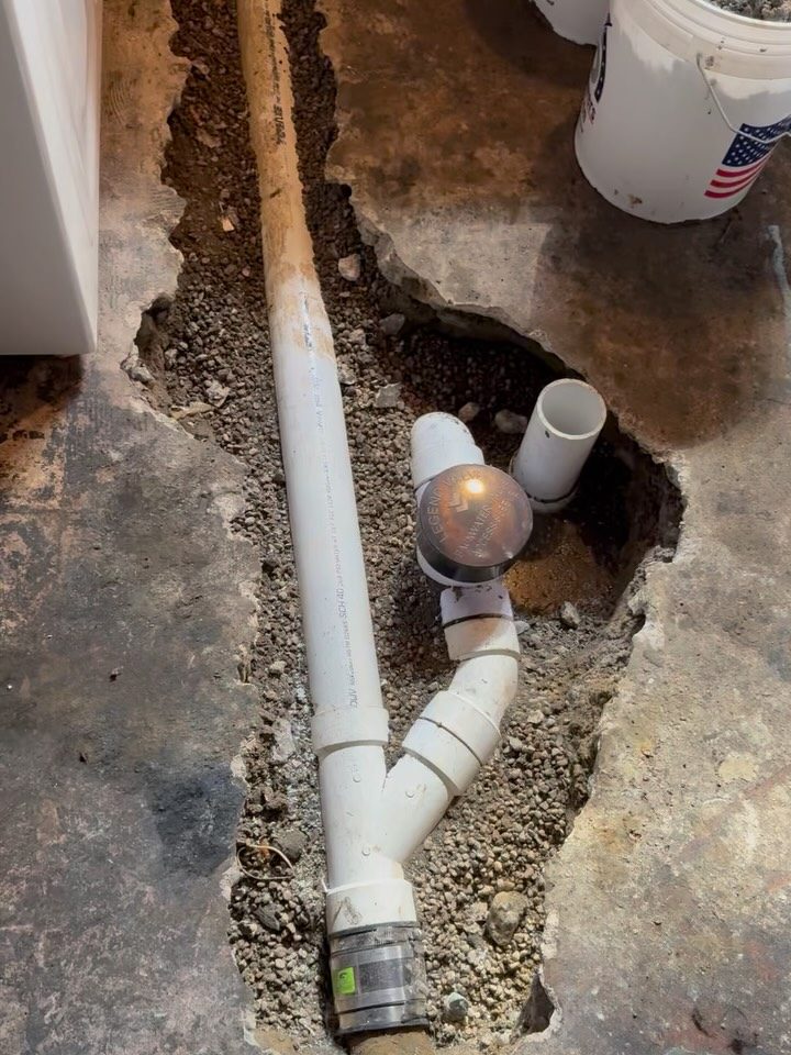 After: new white PVC kitchen drain line laid in the open floor trench with a cleanout