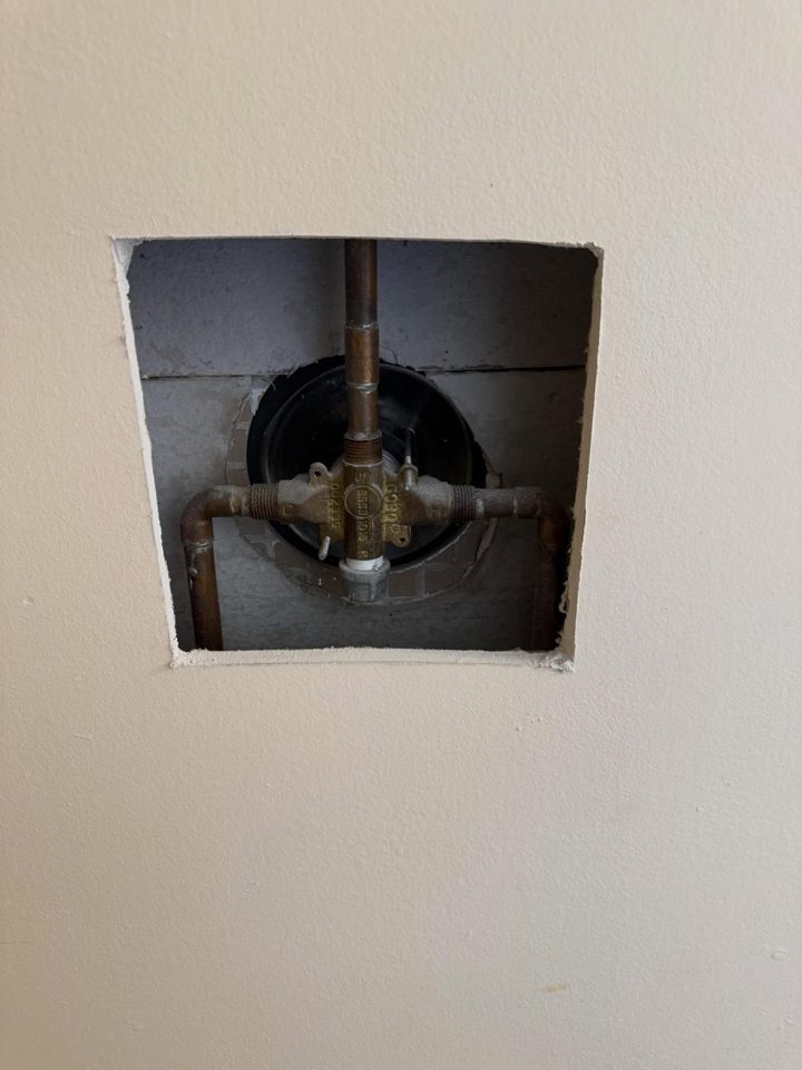 Before: the old shower valve seen through the hole cut in the wall