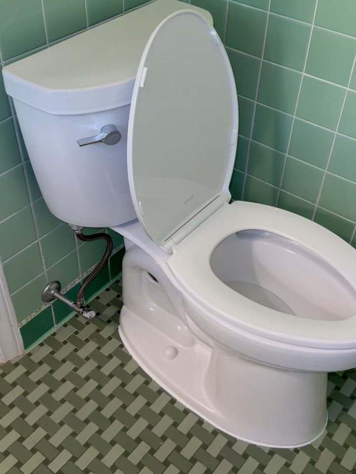 After: new white Kohler Cimarron toilet in a green-tiled bathroom